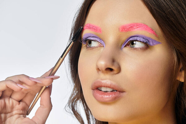 Молодая женщина выставляет напоказ смелые пурпурные тени для век и розовые брови, излучая уверенность.