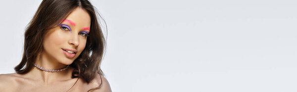 Молодая женщина с яркими фиолетовыми тенями для век и розовыми бровями демонстрирует современную красоту в студии, баннер