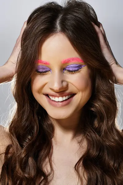 Gülümseyen bir kadın canlı mor göz farları ve pembe kaşlarıyla cesur makyajını sergiliyor..