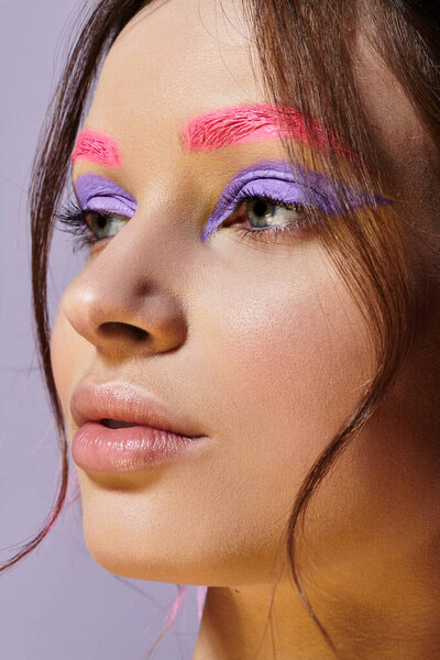 Young woman proudly displays striking purple eyeshadow and vivid pink eyebrows in studio.
