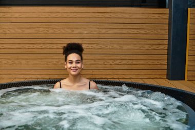 A young african american woman savors the relaxing experience of a spa whirlpool. clipart