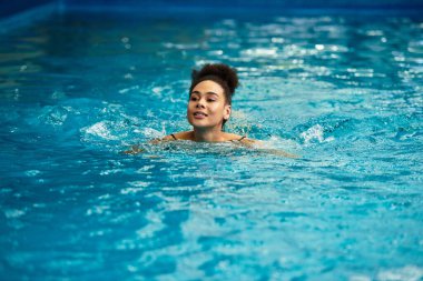 Genç ve şık bir kadın, huzurlu bir spa havuzunun ferahlatıcı suyunun tadını çıkarıyor..