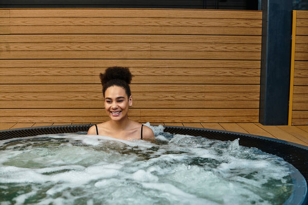 A beautiful young woman is soaking joyfully in a spa, surrounded by soothing water and wooden decor.