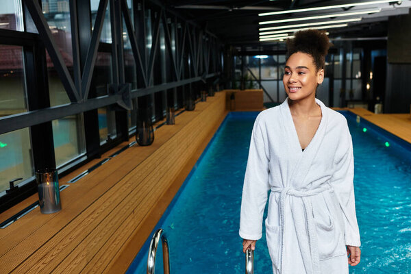 A young chic woman strolls by a tranquil indoor spa pool, embracing relaxation.