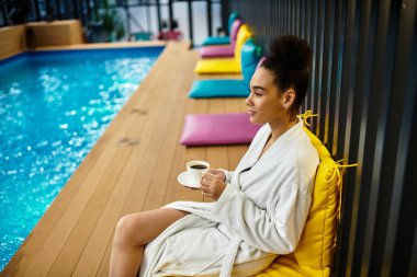 A young African American woman enjoys her coffee while relaxing by a serene pool at a spa. clipart