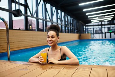 Genç bir Afrikalı Amerikalı kadın, sakin bir spa havuzunda dinlenirken ferahlatıcı bir içkinin tadını çıkarıyor..