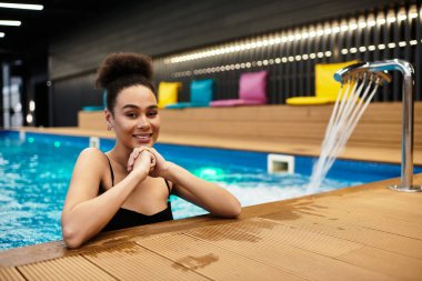 Güzel genç bir kadın huzur dolu bir anın tadını çıkarırken huzur dolu bir spa havuzunda gülümsüyor..