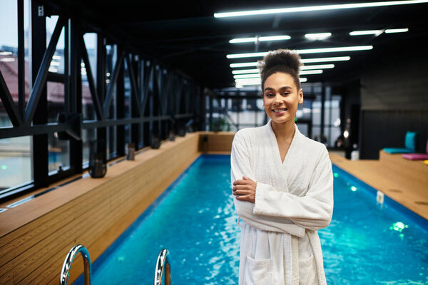 Beautiful young woman smiles confidently while standing by the calming spa pool area during the day.