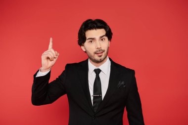 Gösterişli bir takım elbise giymiş karizmatik bir genç adam kendine güvenerek parmağını kaldırıyor..