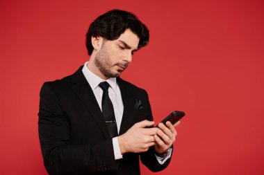 Siyah takım elbiseli genç bir adam akıllı telefonuyla koyu kırmızı bir arkaplana çarpışıyor..