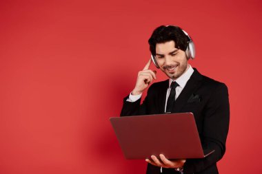 Stylishly dressed brunette man smiles listening to music while using his laptop. clipart