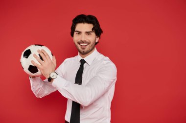 Brunette man in a white shirt and black tie proudly shows a soccer ball with enthusiasm. clipart