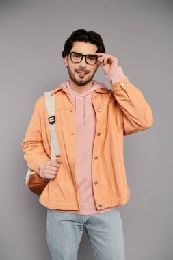 Gözlüklü genç yakışıklı bir adam kendine güveniyor, modaya uygun kıyafetlerini ve çekiciliğini sergiliyor..