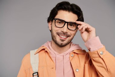 Genç, şık bir adam gözlüklerini ayarlar ve sıcak bir şekilde gülümser..