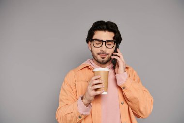 Brunette man wearing glasses holds a coffee cup while engaged in a phone conversation. clipart