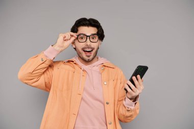 Kumral saçlı, genç, yakışıklı bir adam akıllı telefonunu kullanırken neşe ve şaşkınlık gösteriyor..
