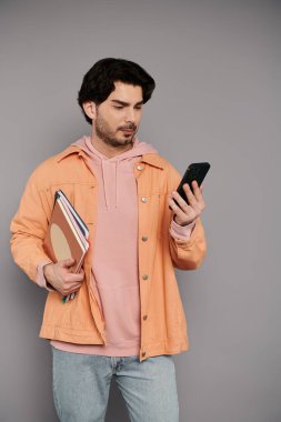 Şık kıyafetli esmer adam defterleri tutuyor ve telefonuna bakıyor, odaklanmış ve rahat..