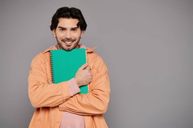 Joyful young man embraces a vibrant notebook, exuding confidence and creativity in a studio setting. clipart