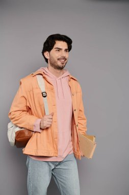 Turuncu ceketli ve pembe kapüşonlu genç bir adam elinde kitaplarla rahatça yürüyor..