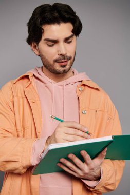 Turuncu ceketli esmer adam ve pembe kapüşonlu adam yeşil defterine notlar yazmaya odaklanıyor..