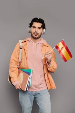 Kulaklıklı genç bir adam canlı bir sahnede İspanyol bayrağı ve renkli kitaplar tutuyor..