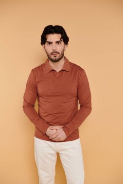 Şık bir genç adam kollarını kavuşturup doğrudan izleyiciye özgüvenle bakıyor..