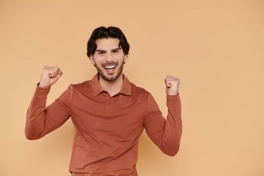 A young man joyfully raises his fists in celebration against a warm backdrop. clipart