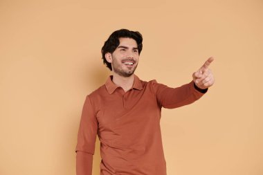 A young brunette man in a stylish orange shirt smiles and gestures with excitement. clipart