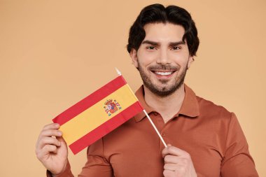 Genç ve yakışıklı bir adam İspanyol bayrağını sıcacık bir arka planda tutarken gururla ışıldıyor..