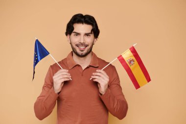 Kahverengi saçlı neşeli bir genç Avrupa ve İspanyol bayraklarını gururla taşıyor..