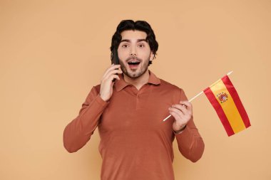 Yakışıklı esmer adam telefonunda İspanyol bayrağı taşıyan neşeli bir anın tadını çıkarıyor..