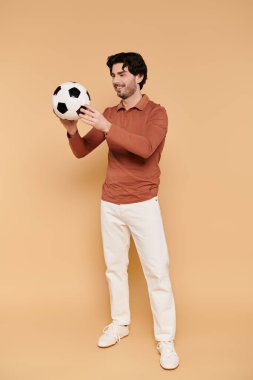 Neşeli genç bir adam neşeli bir şekilde futbol topu tutuyor..