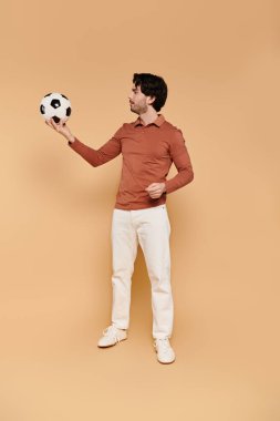 Genç, çekici bir adam, modern bir stüdyoda futbol topunu dengede tutarken kendine güvenerek poz veriyor..