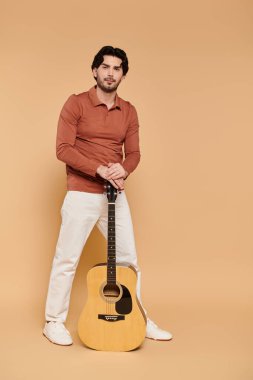 Genç bir esmer adam gitarla ayakta duruyor, cazibesini canlı bir ortamda sergiliyor..