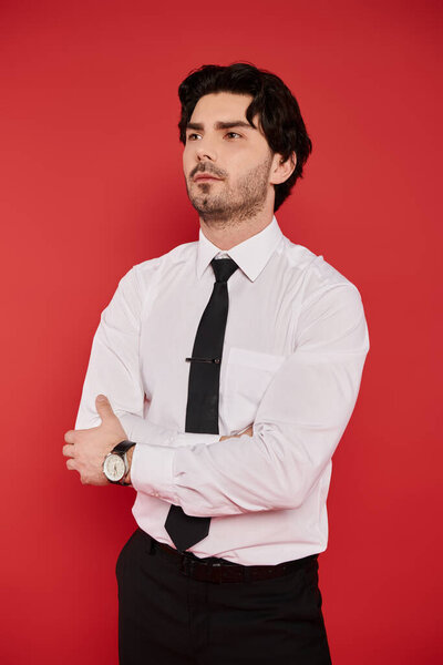 A young handsome man stands with arms crossed, exuding confidence in a well fitted shirt.