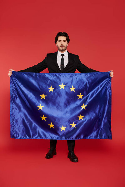 A young handsome man in a suit holds the European Union flag with pride, showcasing unity.