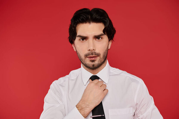 Handsome young man with brunette hair adjusts his tie, exuding confidence and charm.