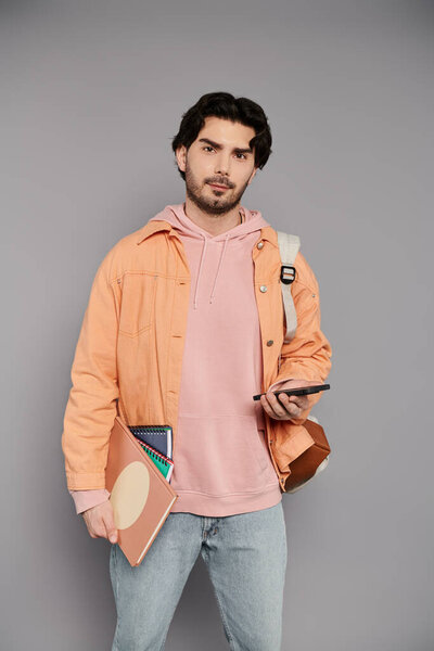 Красивый молодой человек стоит с телефоном и блокнотами, источая расслабленную, но стильную атмосферу.