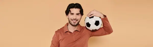 Young man smiles while holding a soccer ball on his shoulder, radiating happiness and energy.