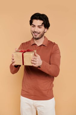 Kahverengi saçlı neşeli genç bir adam elinde güzel bir hediye tutarken heyecanla ayakta duruyor..