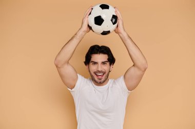 Esmer adam mutlu bir şekilde futbol topunu başının üstüne kaldırır..