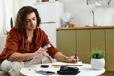 A young man manages his diabetes while recording blood sugar levels at home. clipart