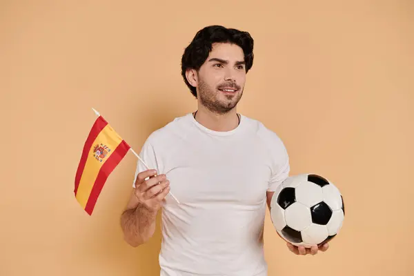 A young handsome man holds a soccer ball and a flag, showing his passion for sports and pride.