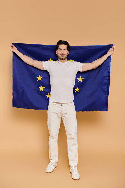 A young man with brunette hair stands confidently, displaying the European Union flag with pride.