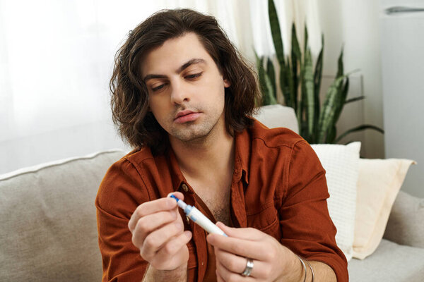 Белый мужчина с длинными волосами фокусируется на инсулиновой ручке, размышляя о своем здоровье.