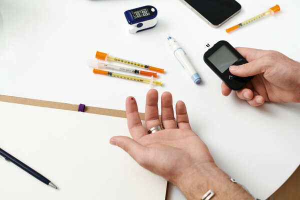 Young man checks blood sugar with a meter while surrounded by diabetes management tools at home.