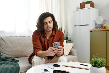 Modern bir dairede, genç bir adam diyabet ve günlük yaşamla uğraşırken telefonunu kontrol ediyor..
