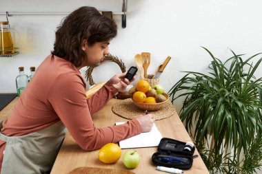 Odaklanmış genç bir adam kan şekeri seviyelerini izliyor ve şık mutfağındaki ayrıntıları not ediyor..