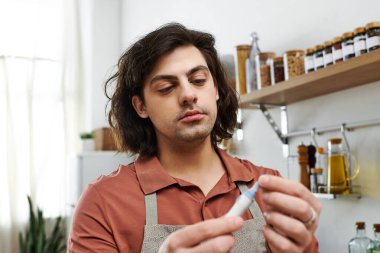 Şık bir dairede, genç bir adam sağlığını korurken insülin kalemini inceler..