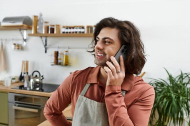 Güzel görünümlü, uzun saçlı genç adam şık mutfağında telefonla konuşuyor..